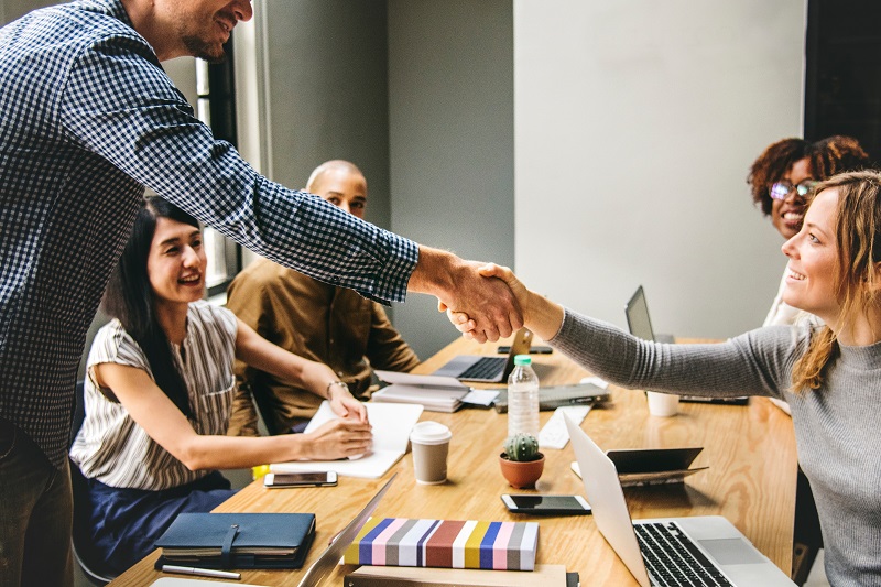 people seated around a table for a meeting, and two people shaking hands