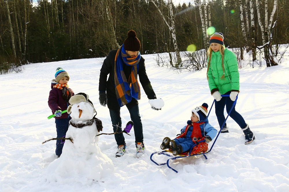 image of family playing in the snow with a sled and making a snowman