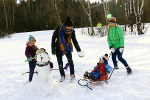 Photo of two children and their parents playing in the snow with a snow man and sled