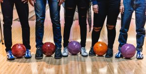 image of 5 people (legs only) standing with a bowling ball between their feet