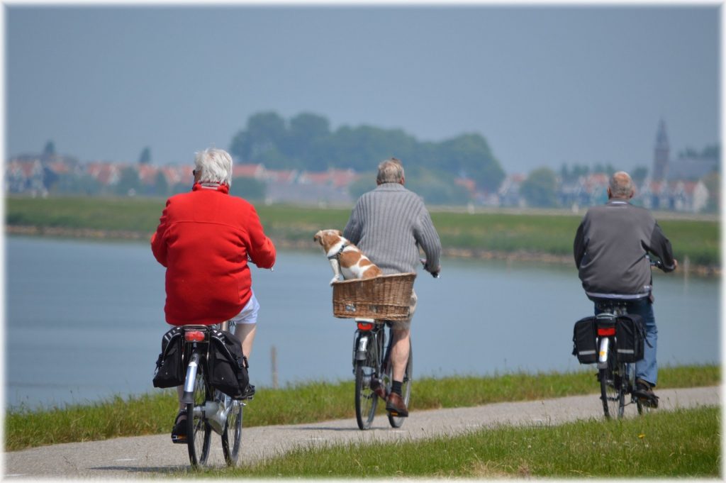 three seniors riding bicycles along a pathway along a body of water.