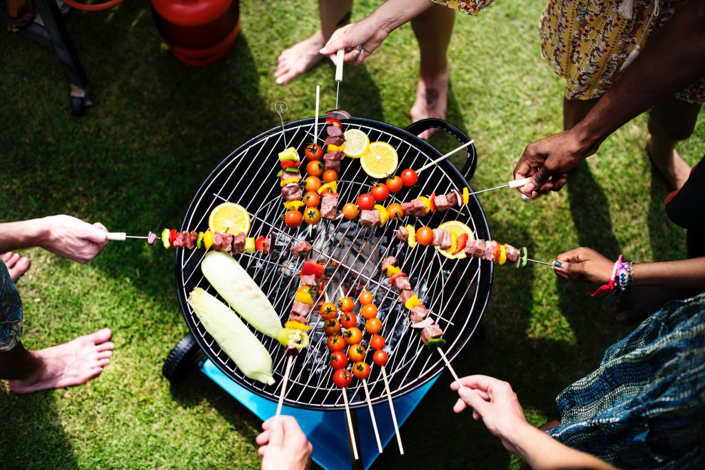 several people standing around a BBQ with skewers on the BBQ