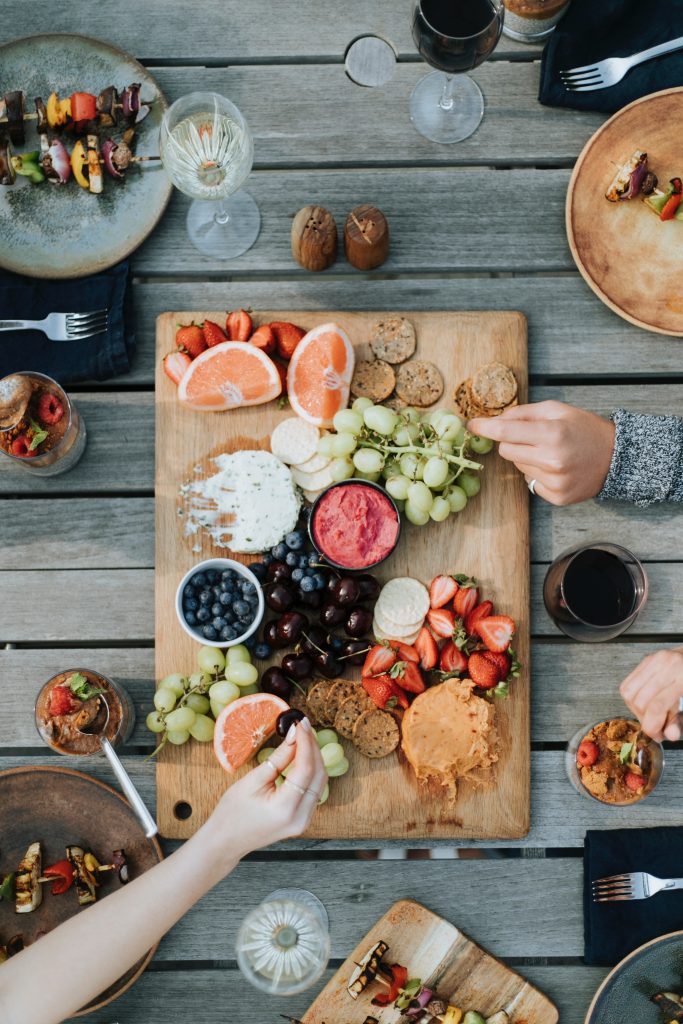 photo of table with a spread of food and hands reaching for food.