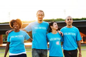 4 people standing with their arms around one another, all wearing blue t-shirts that say "volunteer"