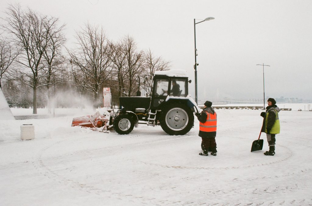 a snow removal tractor in a parking lot with two people holding shovels standing nearby