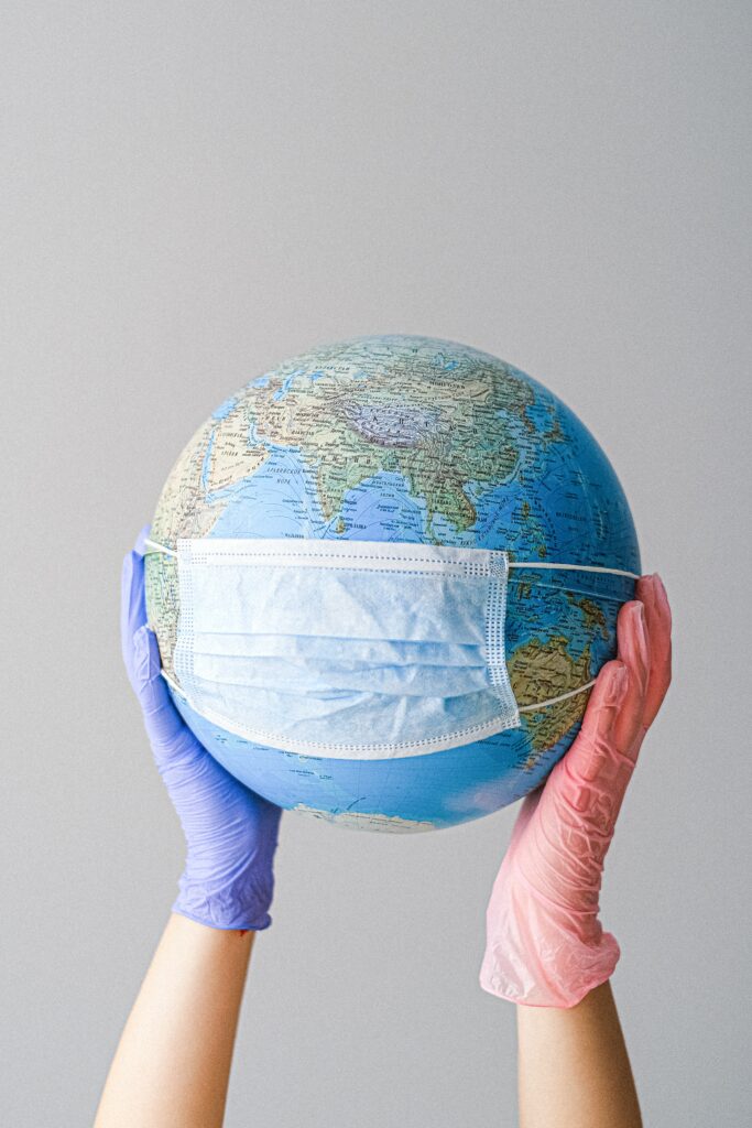 gloved hands holding a globe and the globe is wearing a mask