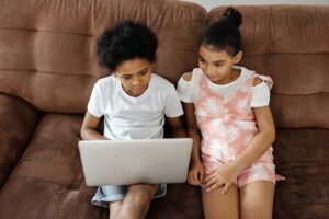 two children sitting on a couch looking at a laptop