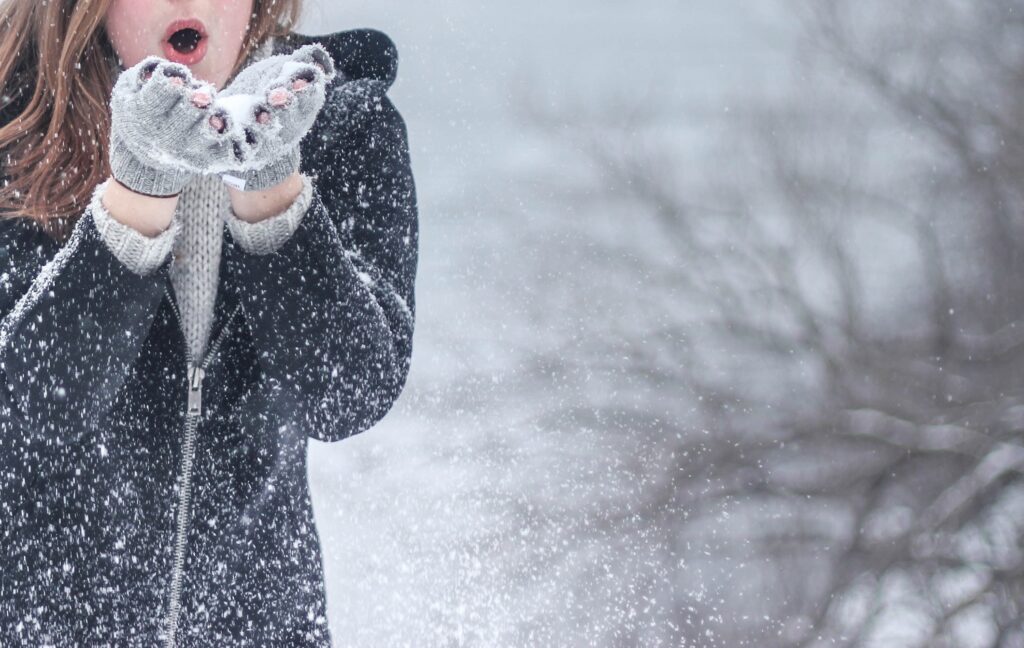 woman blowing snow off her mittens