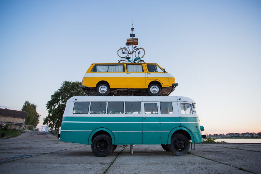 a stack of vehicles: a bicycle on top of a scooter on top of a van on top of a bus