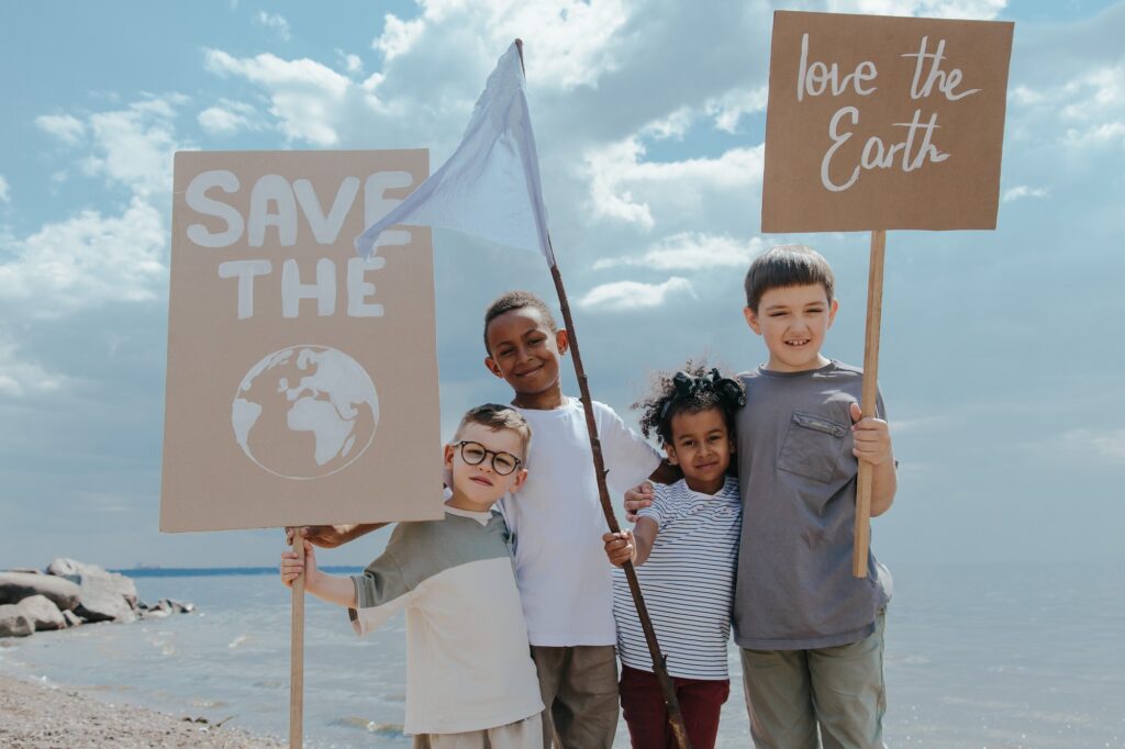 Four kids under 10 years old who are on a beach and holding signs saying "save the earth" and "love the earth"