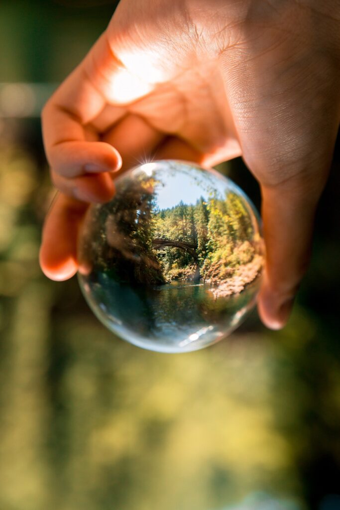 a person holding a glass orb that is reflecting a beautiful nature scene - a river, trees, etc.