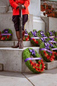a photo of an RCMP in uniform standing at a memorial statue with a number of Remembrance Day wreaths on display.