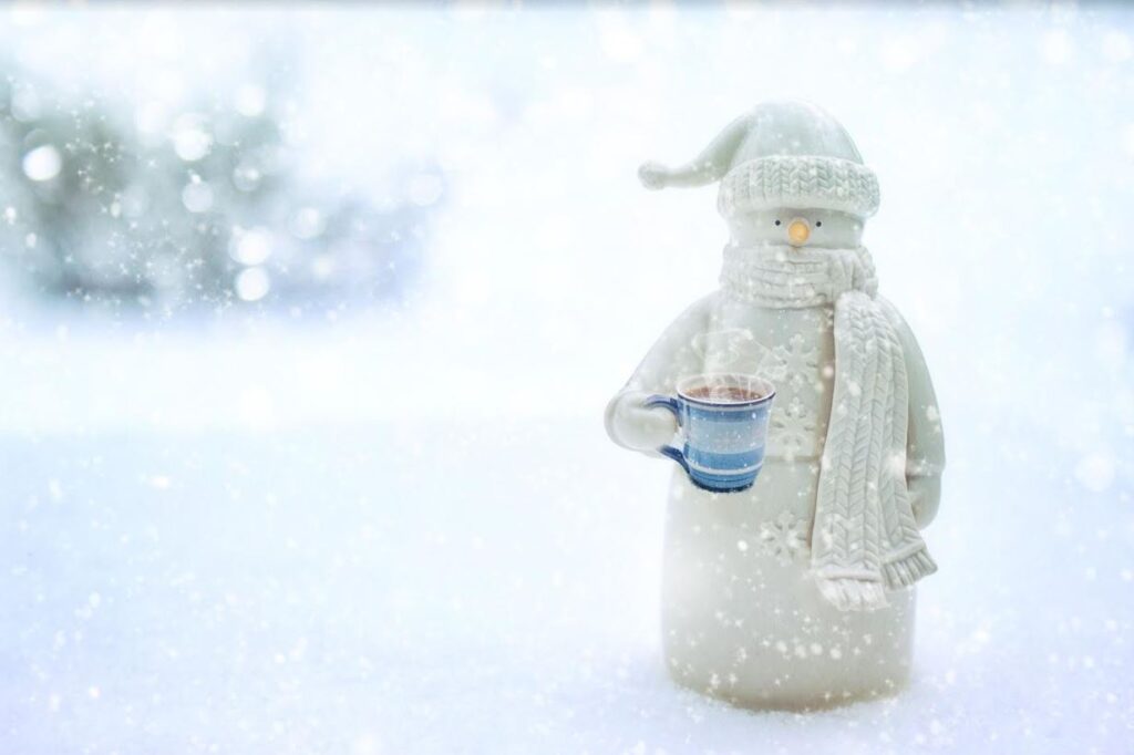 snowman figurine holding a cup of steaming hot chocolate while outside in the snow