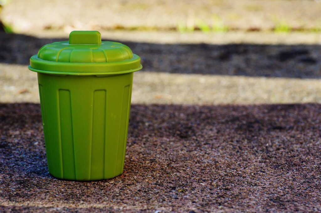 an image of a toy green garbage bin sitting on a dirt surface