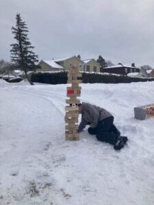 a person playing with a jumbo jenga game outdoors in the snow at the winter carnival / une personne jouant avec un jeu de jenga jumbo en plein air dans la neige lors du carnaval d'hiver