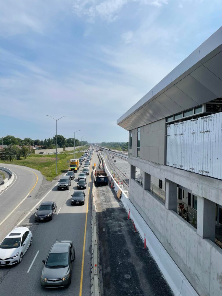 Photograph showing the impact of the construction on traffic along the 174.  You can see a station under construction to the right of the photo and then down below you see cars lined up and moving slowly in the two open lanes for traffic.
