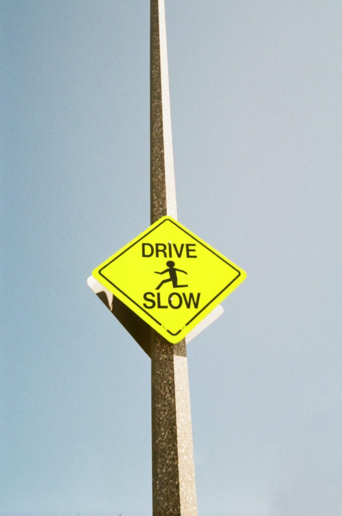 A photo of a bright yellow sign that says "drive slow." The sign is attached to a stone pole. The sky in the background is blue.