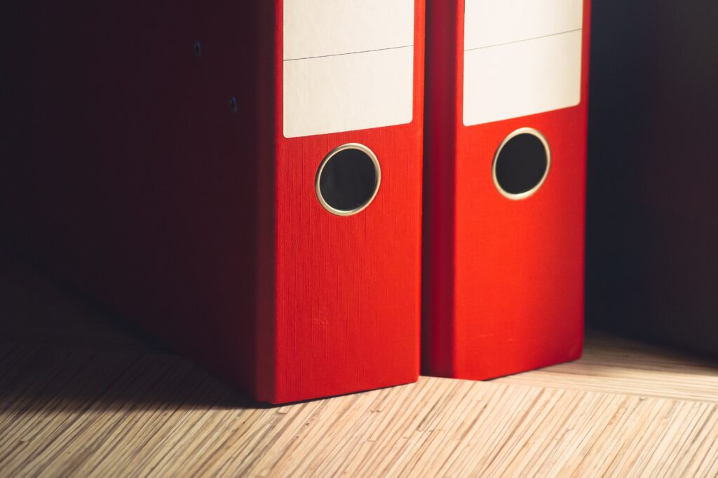 A pair of red filing binders sitting on a wooden surface.