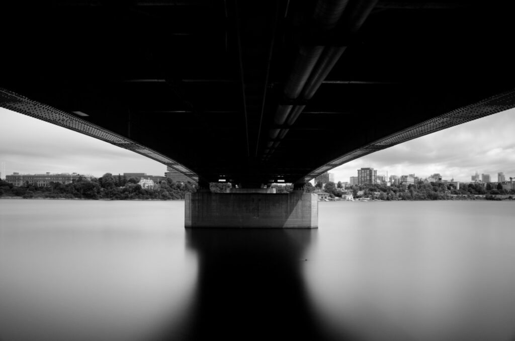 Black and whilte photograph of the underside of the Macdonald Cartier Bridge crossing the Ottawa River.