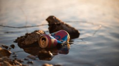 an empty aluminum can sitting on some rocks at the edge of some water.