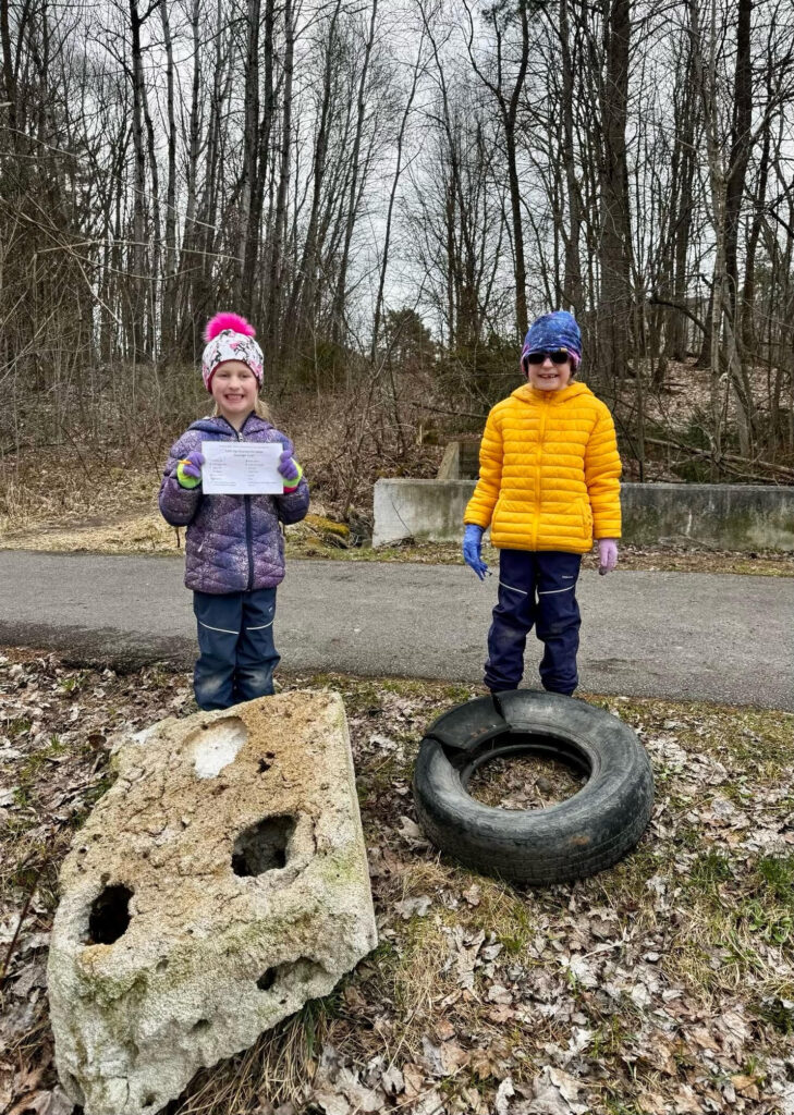 A photo showing two young community members at the clean up. They are standing behind two large unusual pieces of trash - a large chunk of concrete and an old tire.