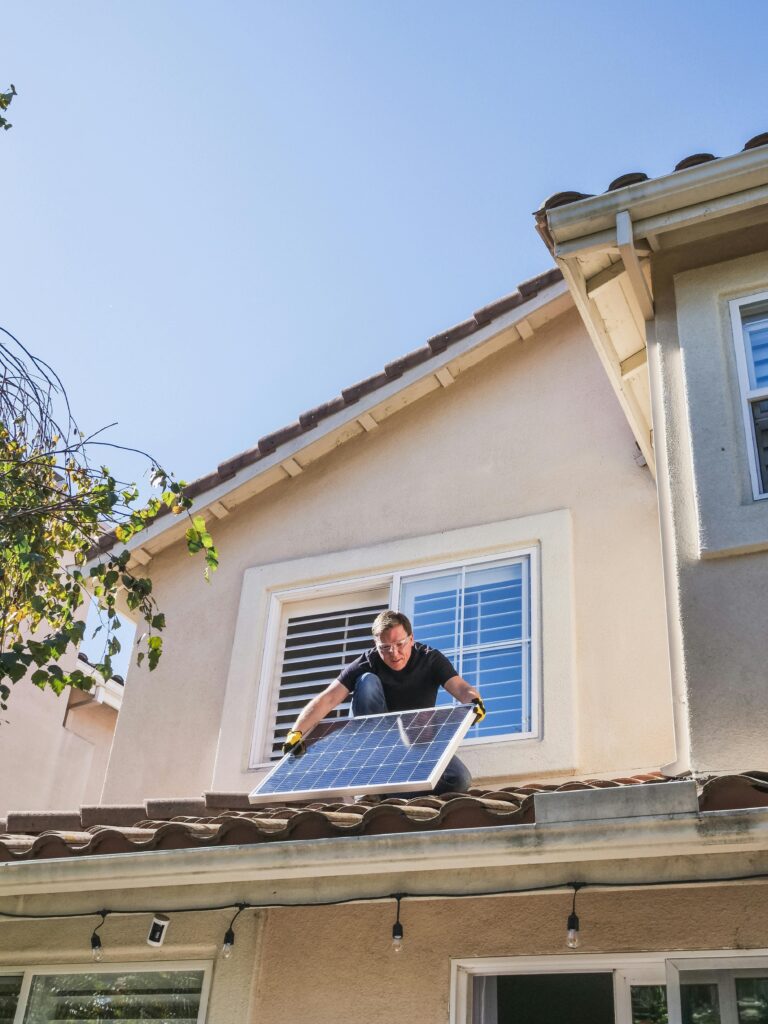A man installing a small solar panel on a lower roof of a home.