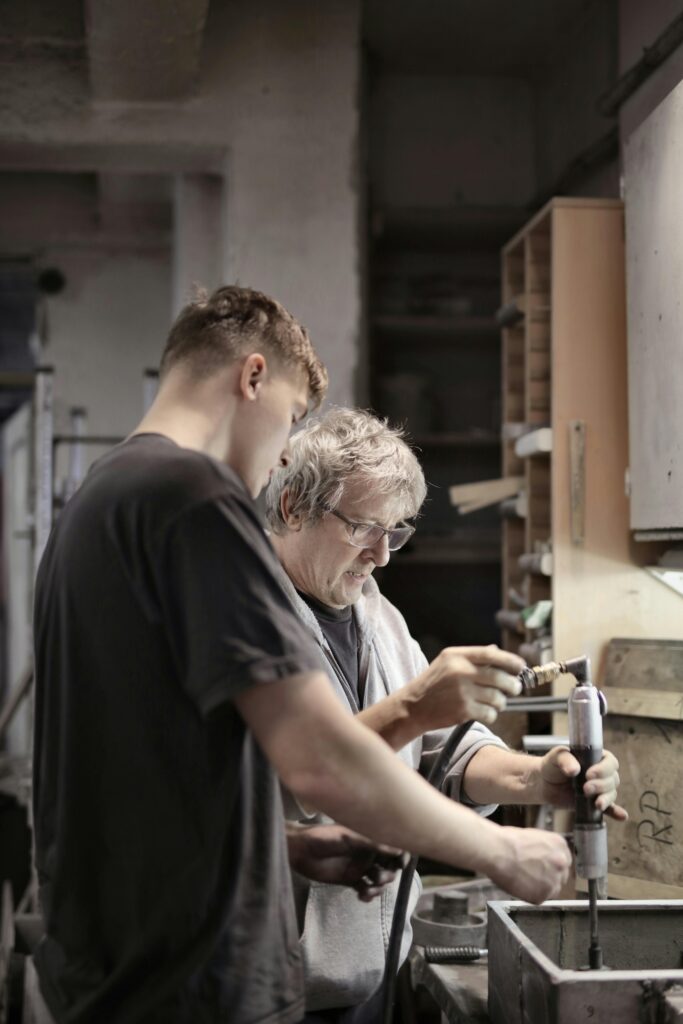 A photo of a younger man and an older man working together over a sink using a tool.